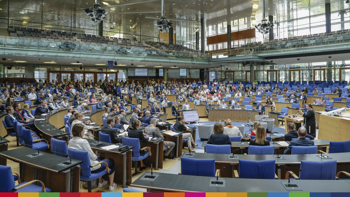 Mehrere politische Entscheidungsträger:innen sind in einem Plenarsaal versammelt