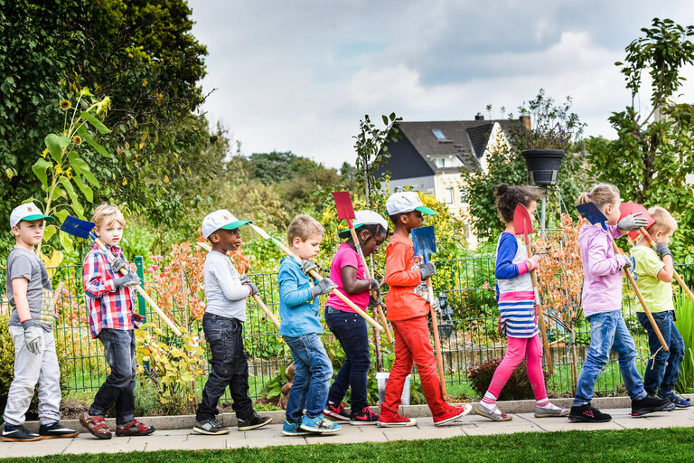 Mehrere bunt gekleidete Kinder gehen vor einer Grünanlage entlang. 