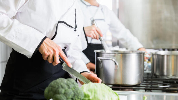 Das Bild zeigt die Hände eines Kochs, der Gemüse schneidet.