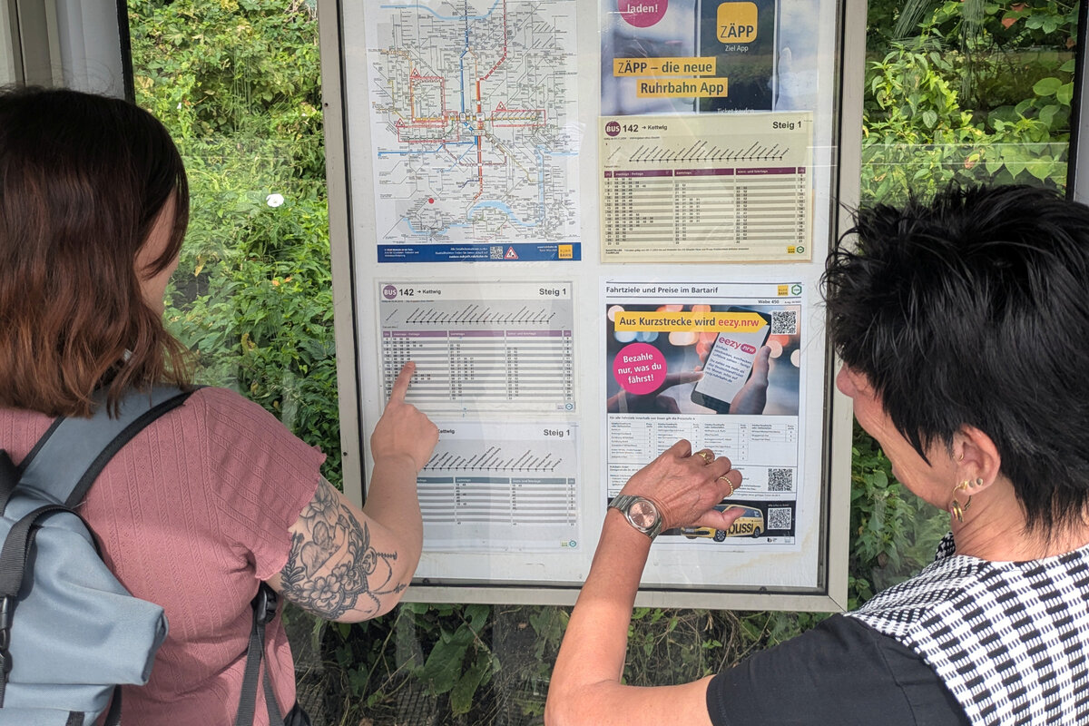 Zwei Frauen stehen am Abfahrtsplan in einer Bushaltestelle
