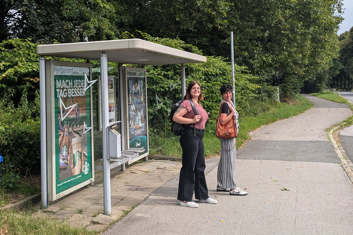 Zwei Frauen stehen an einer Bushaltestelle